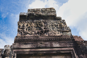 Stone carving depicting apsara dancers performing traditional khmer dance, adorning the ancient sandstone architecture of a temple ruin in the historical angkor complex against a blue sky