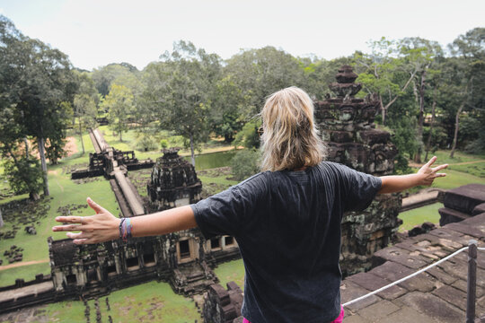 Young woman standing on top of an ancient temple, spreading arms enjoying the freedom and panoramic view of the vast archaeological park and surrounding jungle in cambodia