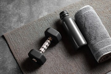 black dumbbell, water bottle, and towel on a mat against a grey background with copy space for a gym or fitness concept.
