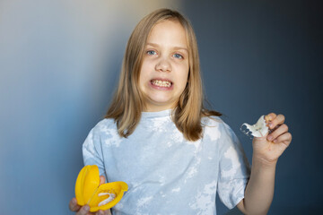 Young child holding a banana peeler and a banana peel with a confused expression at home during daytime