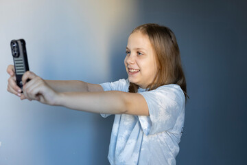 Child taking a selfie with a smartphone while smiling in a simple indoor setting
