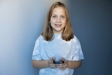 Girl smiling while holding a smartphone in a well-lit room with a blue background during daytime