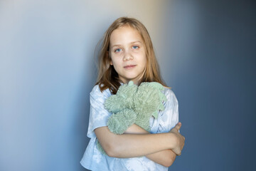 Girl holding a green stuffed animal poses against a simple blue background in a calm indoor setting
