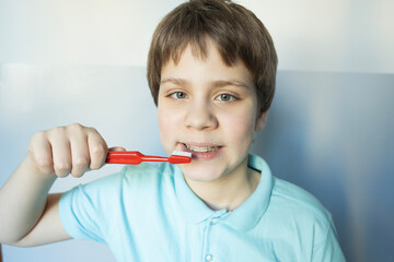 Young boy brushes teeth in light blue shirt, promoting good dental hygiene practices at home during daytime