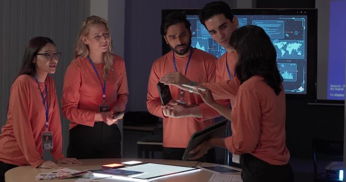 Product team in matching orange shirts collaborates around table, reviewing wireframes, color swatches, mobile app prototypes with analytics dashboards. Capturing UX UI sprint planning session
