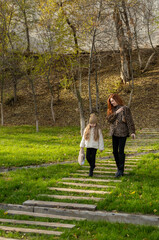 Mother and daughter walking on wooden path through autumn park. Warm clothes, plush toy, peaceful moment.