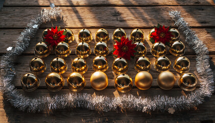 Golden Christmas bells and festive decorations arranged on a rustic wooden table with silver tinsel and red flowers.