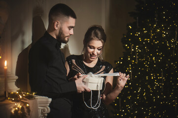 A loving couple opens Christmas and New Year's gifts near a Christmas tree.