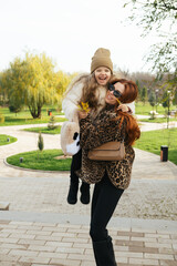 Mother and daughter walking hand-in-hand through a landscaped park in cool weather. Autumn vibes, warm clothes, peaceful moment.