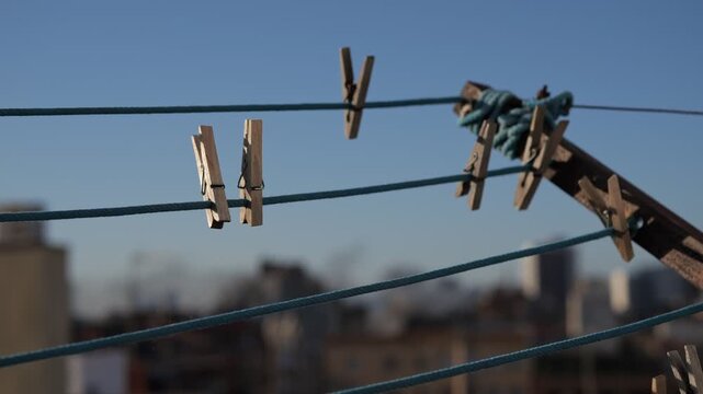 Clothespins hanging on a clothesline against a clear blue sky. The background features blurred buildings, creating an urban atmosphere.