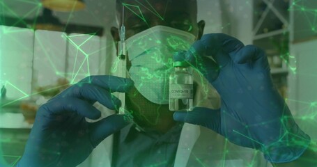 Presenting worker in lab coat, surgical mask and gloves holding syringe and COVID-19 vial at clinic