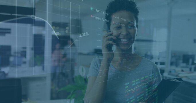Talking woman in short-sleeve top holding clipboard and smartphone in office with charts overlay