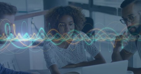 Reviewing three-person team leaning over laptop in office, woman in white eyelet blouse, waveform