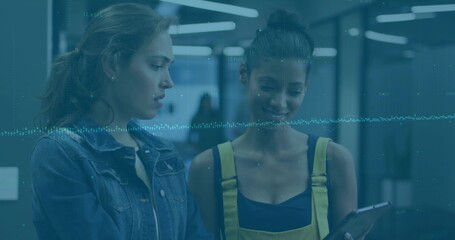 Viewing two coworkers in denim jacket, yellow overalls checking tablet in office corridor, waveform