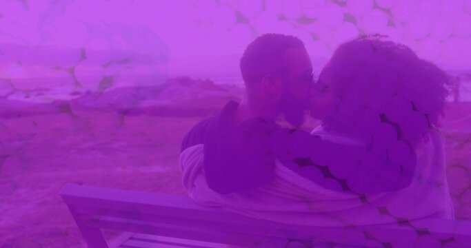 Kissing couple on wood bench hugging and wrapping in light blanket, man with shades, purple overlay