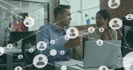 Discussing man in blue shirt, woman in sweater examining laptop at desk in office, network overlay