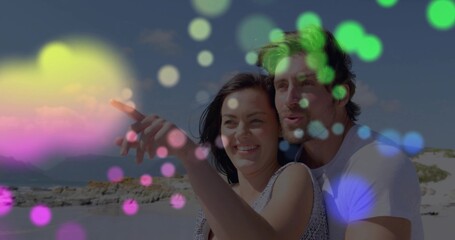 Pointing sleeveless woman and tee-clad man holding, gazing at horizon on rocky shore, with bokeh