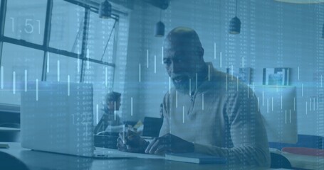 Working man wearing sweater typing on laptop at modern office desk, with notebook and data overlay