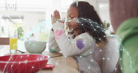 Praying girl in knit sweater closing eyes and folding hands at dining table, digital mesh overlay