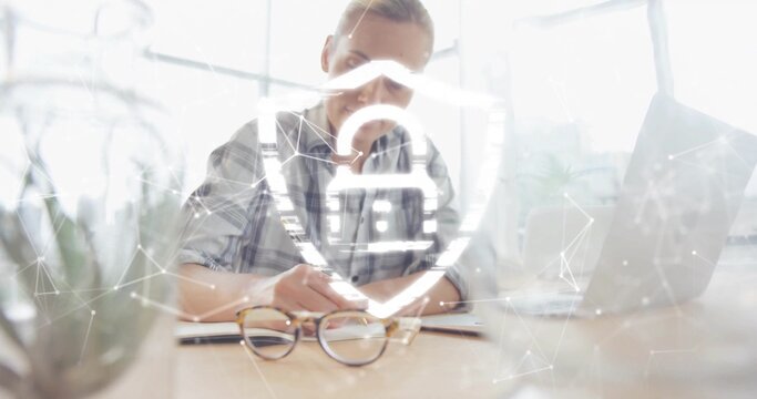 Writing woman in plaid shirt leaning at modern desk, marking notepad with digital shield overlay