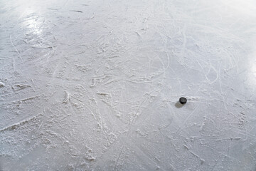 An ice hockey puck in the goal, on textured ice with skate tracks.