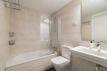 Modern bathroom with a shower and bathtub. White tiles cover the walls. A sink with a mirror is visible. Clean and minimalistic design.