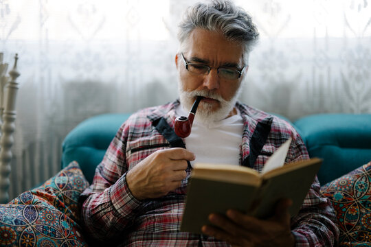 Elderly man enjoying a book and smoking a pipe