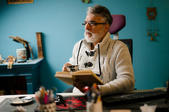 Elderly man enjoys reading a book while sipping tea