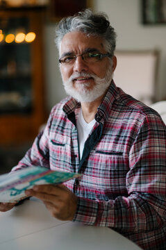 Elderly man with silver hair smiles while holding a magazine