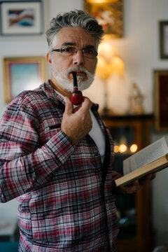 Man reading a book and holding a pipe in a cozy indoor