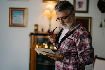 Older man reads a book while holding a pipe