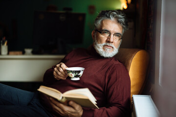 Senior man enjoying a warm drink while reading a book