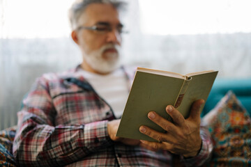 Senior man reading a book indoors on a cozy sofa