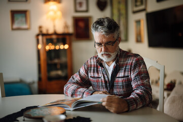 Senior man reading a magazine at a cozy home setting
