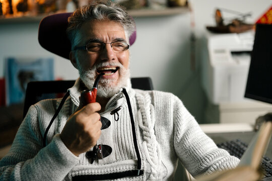Smiling elderly man enjoying a pipe while reading