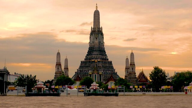 Wat Arun, also known as the Temple of Dawn, stands tall by the river in Bangkok, Thailand. The stunning architecture reflects the vibrant hues of the sunset, creating a picturesque view.