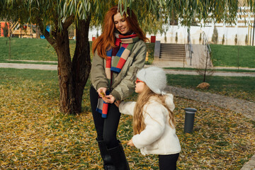 Mother and daughter exploring autumn park, surrounded by yellow leaves. Cozy outfits, playful moment, seasonal bonding outdoors.