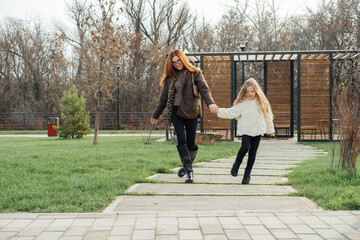 Mother and daughter walking on wooden path through autumn park. Warm clothes, plush toy, peaceful moment.