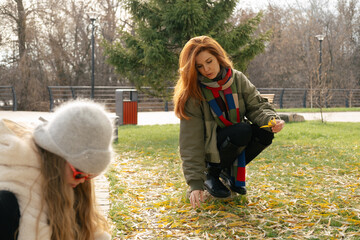 Mother and daughter exploring autumn park, surrounded by yellow leaves. Cozy outfits, playful moment, seasonal bonding outdoors.