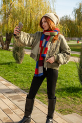 A young woman enjoying a sunny autumn or winter day outdoors, taking a cheerful selfie on a paved path in a park. Making photo.