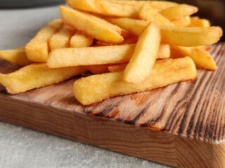 Golden crispy French fries on old wooden board on table in cafe. Potatoes lightly sprinkled with salt. Close-up.