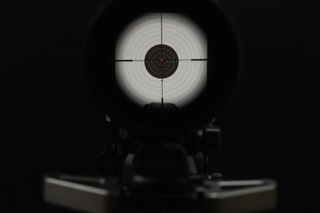 View through rifle scope with crosshairs aiming precisely at the center of a paper shooting target on black background