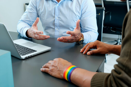 man explaining medical care options to young Black woman at desk with laptop, both gesturing with hands during consultation in clinical office setting