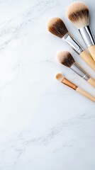A collection of four makeup brushes with natural wooden handles and silver ferrules are arranged on a white marble surface. The lighting is bright and clean, hi