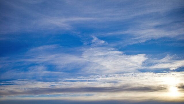 Soft cirrus clouds stretch across a blue sky at sunset, creating a calm and airy natural background.