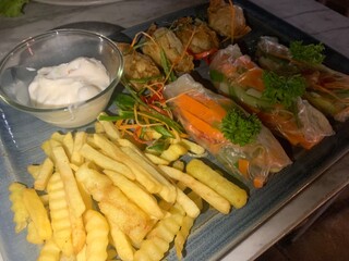Platter of appetizers Spring Rolls cuisine combination fresh spring rolls and fried wontons served with french fries and dipping sauce, Three translucent rice paper are visible various vegetables.