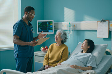 Black man doctor holding clipboard talking to senior Asian woman and young Asian woman lying in hospital bed during medical care visit in patient room