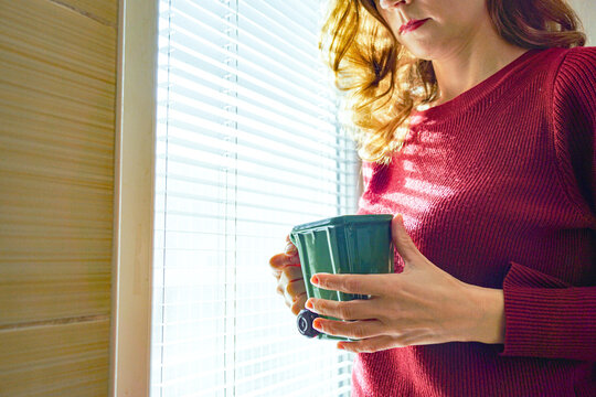 Female hands gripping a garbage-container coffee cup near sunlit window blinds. Symbolizes environmental conversation starter, recycling advocacy through design, and waste sorting discussion prompt.