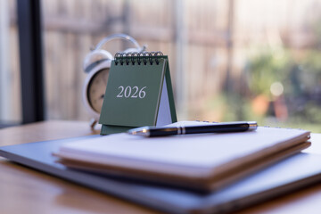 2026 desk calendar with notebook, pen, and clock on wooden table in cozy daylight workspace, perfect for planning productivity, and time management content. © Smallroombigdream