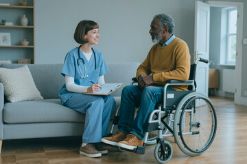 Obraz premium female nurse sitting on sofa talking to senior Black man in wheelchair holding clipboard and pen providing medical care in modern healthcare setting